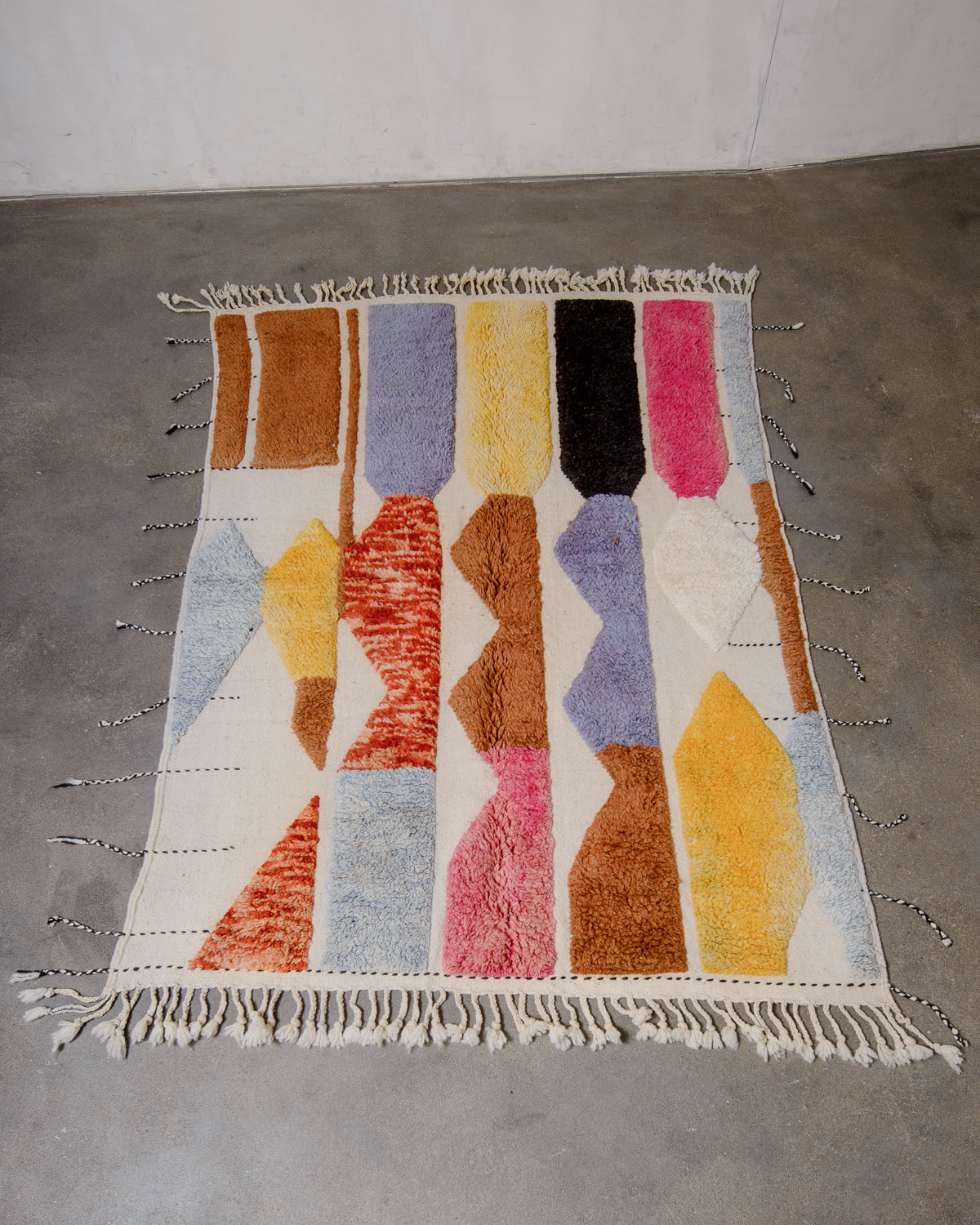Berberlin Beniourain rug in colourful wool and cream, laying flat on concrete studio floor.